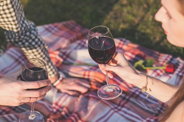 Auf der Wiese liegt eine Decke und zwei Personen trinken Wein.