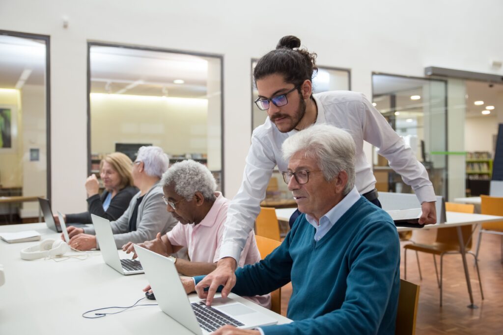 Junger Mann hilft älteren Männern, die vor Laptops sitzen