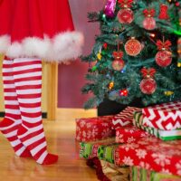 Kinderbeine stehen vor einem Weihnachtsbaum und Geschenken