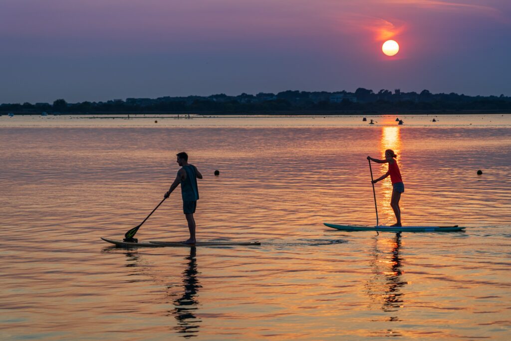 Stehpaddler auf einem See bei Sonnenuntergang.