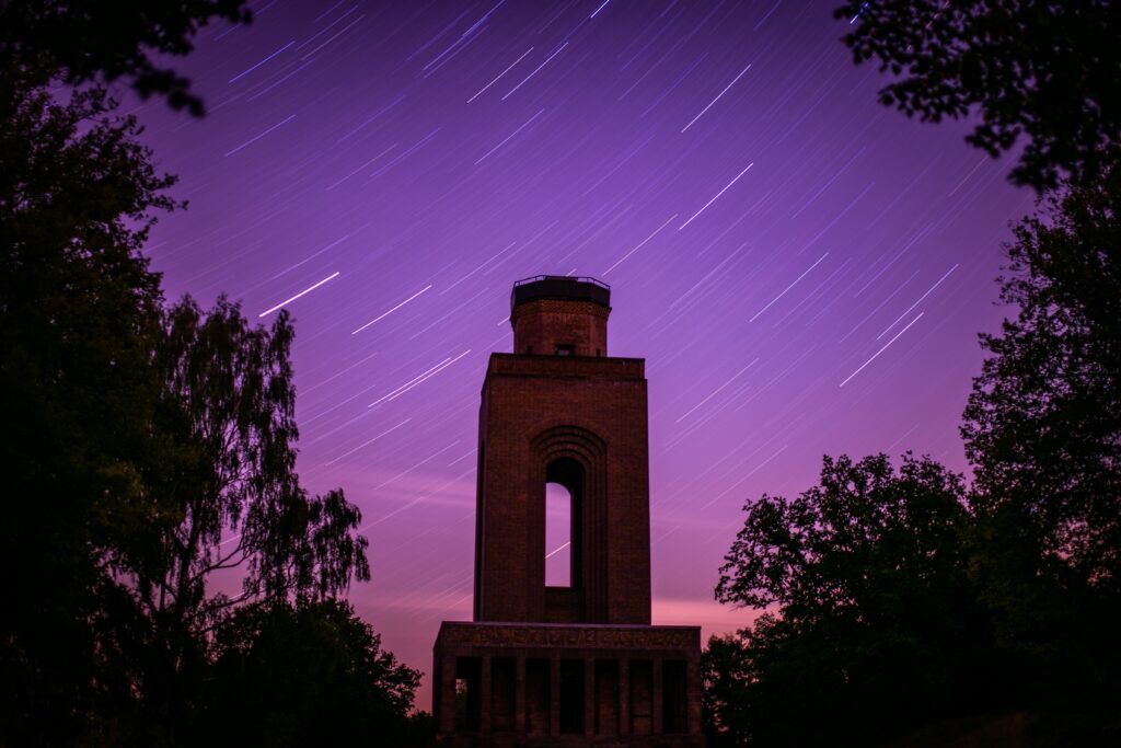 Ein Turm vor einem pinken Himmel voller Sternschnuppen.