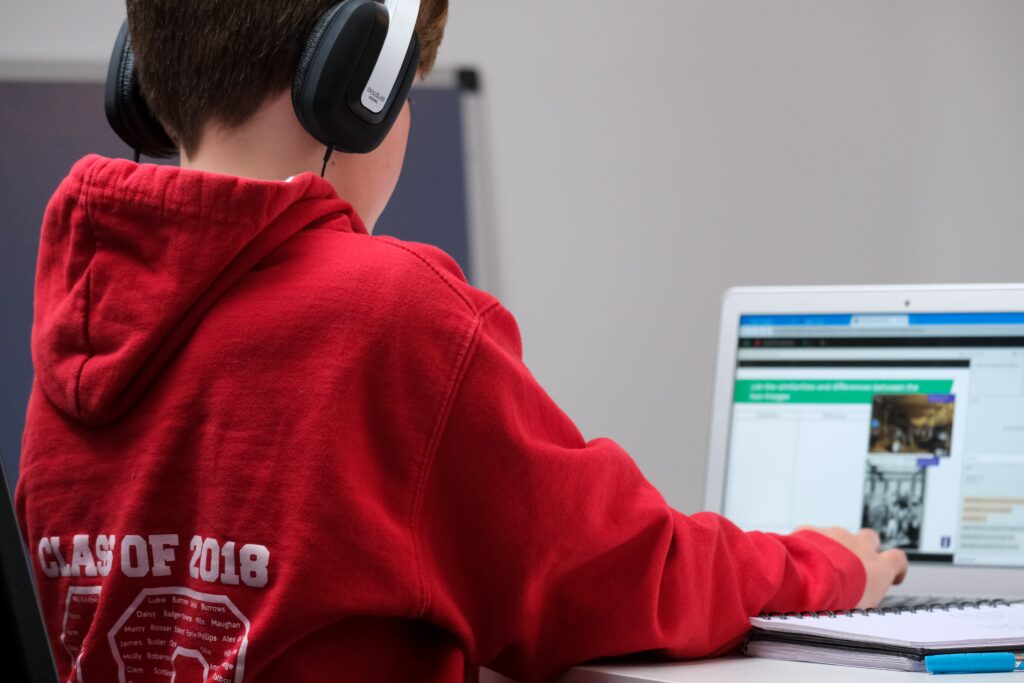 Junge in rotem Pullover sitzt mit Kopfhörern vor einem Laptop
