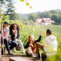 Eine Familie sitzt nach einem Wanderausflug an einem Weinhang und genießt den Tag des offenen Weingutes im Elbland.