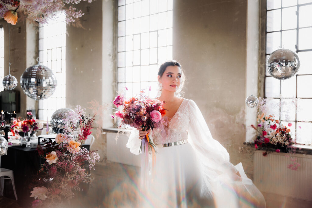 Eine Braut steht mit farbenfrohem Blumenstrauß in einem hellen und detailreich dekorierten Raum.