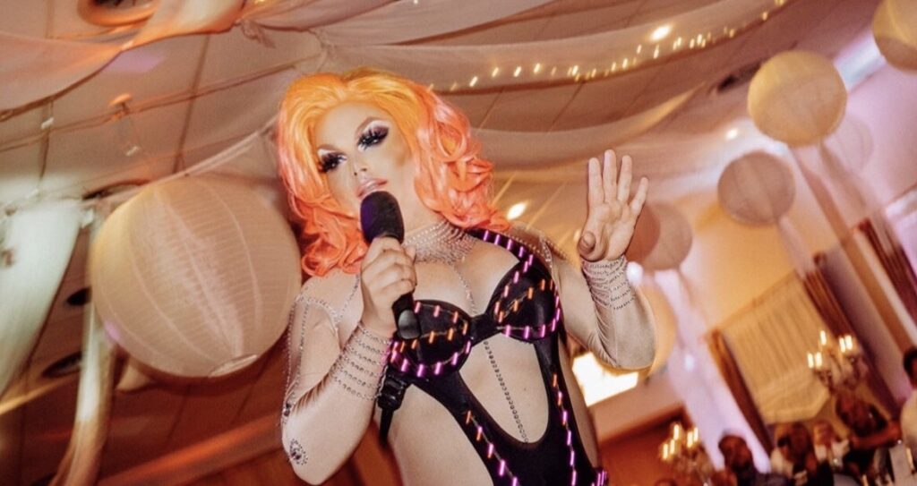 Debbie mit Mikrofon und orangener Perücke bei einem Auftritt.