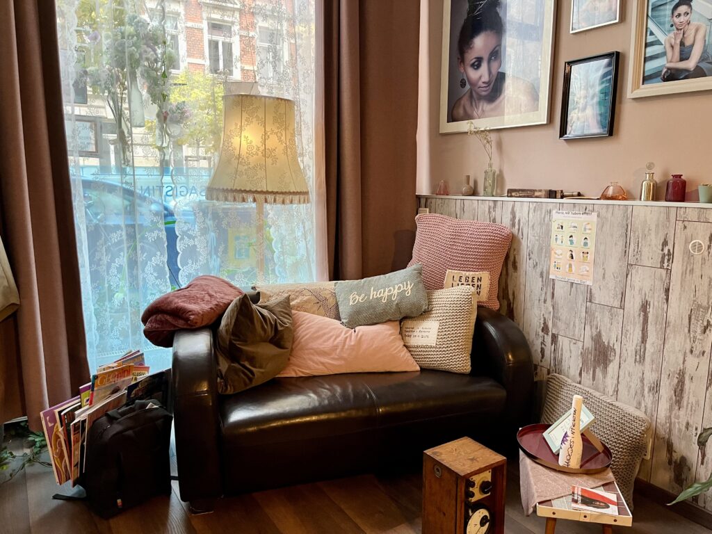 Braunes Sofa mit vielen bunten Kissen, gemütliche Lampe vor großem Fenster