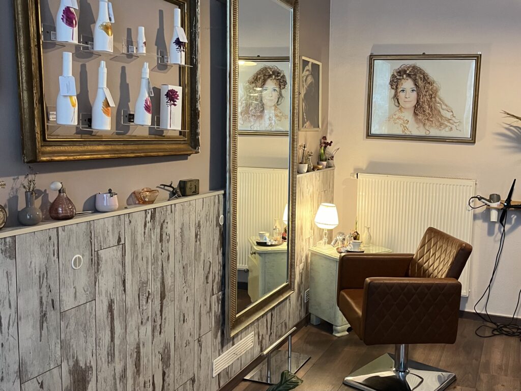 Friseursalon Nadine Kaiser, Haarpflegeprodukte aufgereiht, großer Wandspiegel, gemütliches Licht, gemütlicher Frisierstuhl