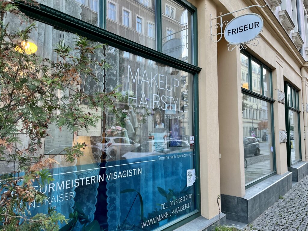 Friseursalon Nadine Kaiser im Dresdner Hechtviertel von außen: große Fenster, mit weißen Gardinen und einladender Fensterdekoration