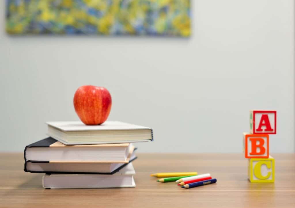 Ein Stapel Bücher, Buntstifte und ein Apfel auf einem Tisch