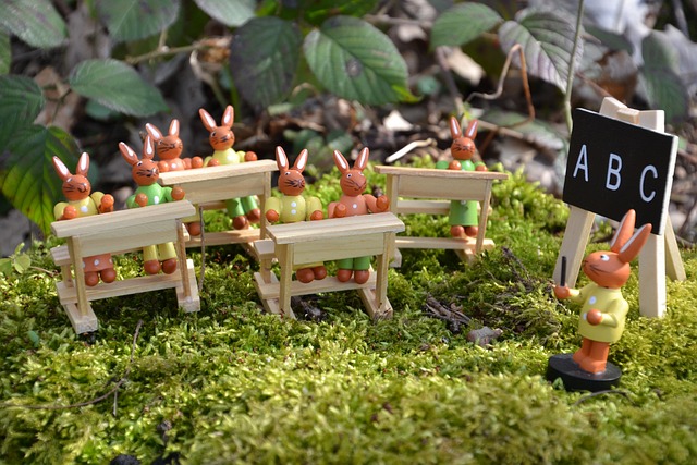 Holzfiguren, kleine Hasen sitzen auf Schulbänken inmitten von grünem Moos