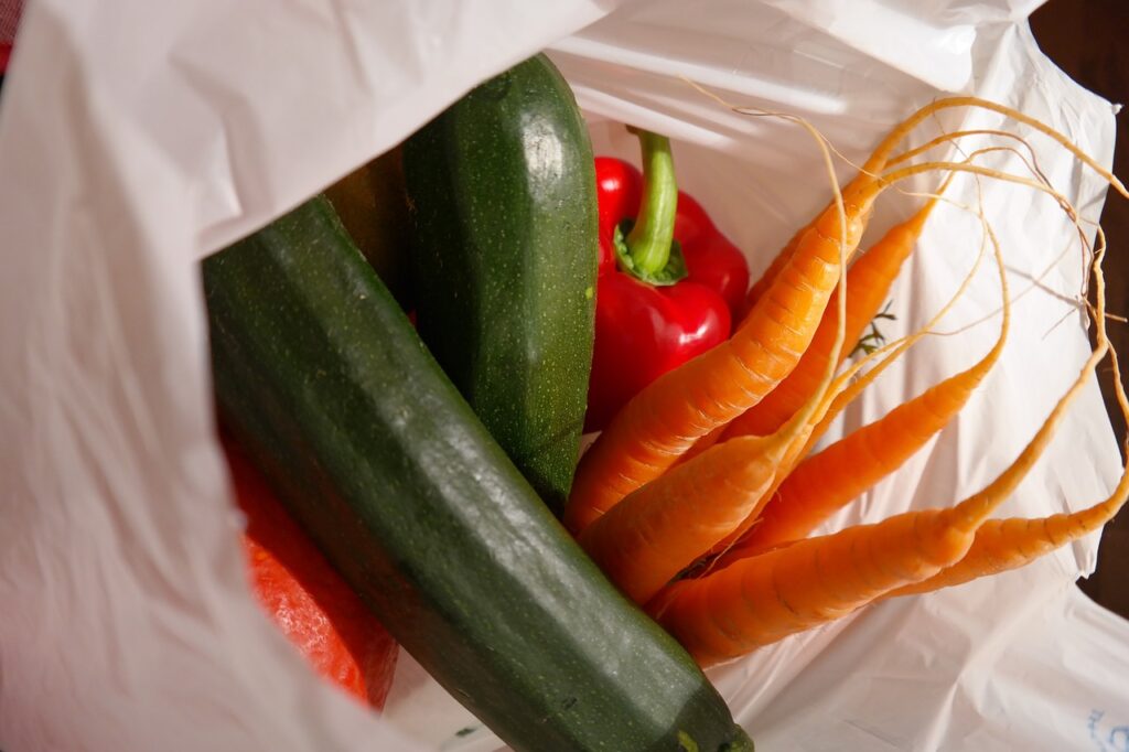 In einer weißem Plastiktüte liegen zwei Zucchini, eine rote Paprika und sechs Karotten.