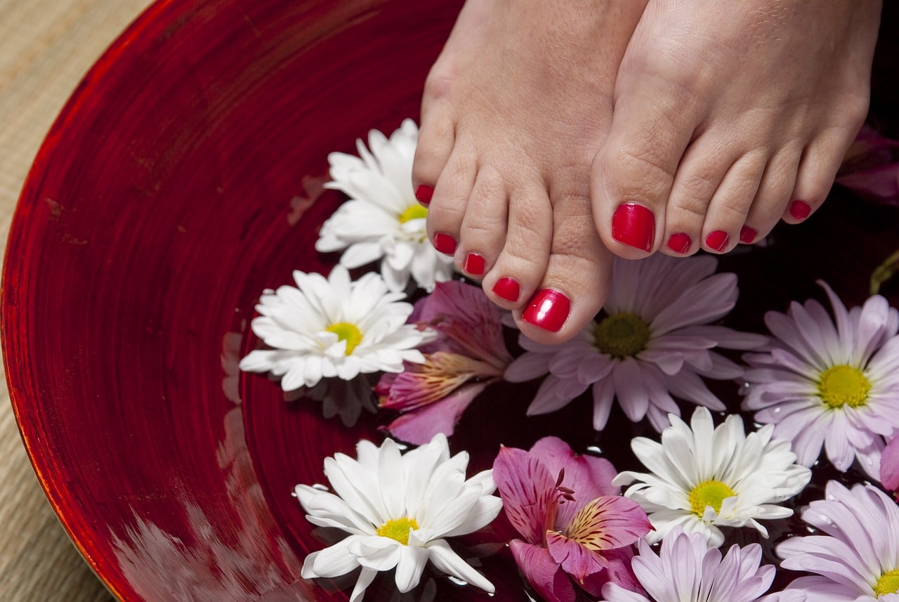 Füße mit rotem Nagellack über einer Schüssel mit Wasser und bunten Blüten