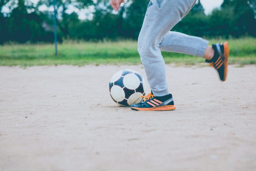 Jugendliche Person kickt mit rechtem Fuß gegen einen blau-weißen Ball