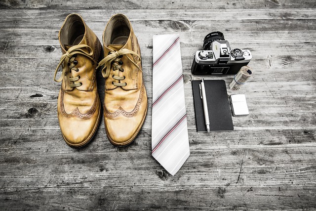 Vintage, braune Herrenschuhen, daneben eine weiße Krawatte mit rotenStreifen, eine alte Kamera, ein schwarzes Notizheft mit Stift und eine Geldrolle
